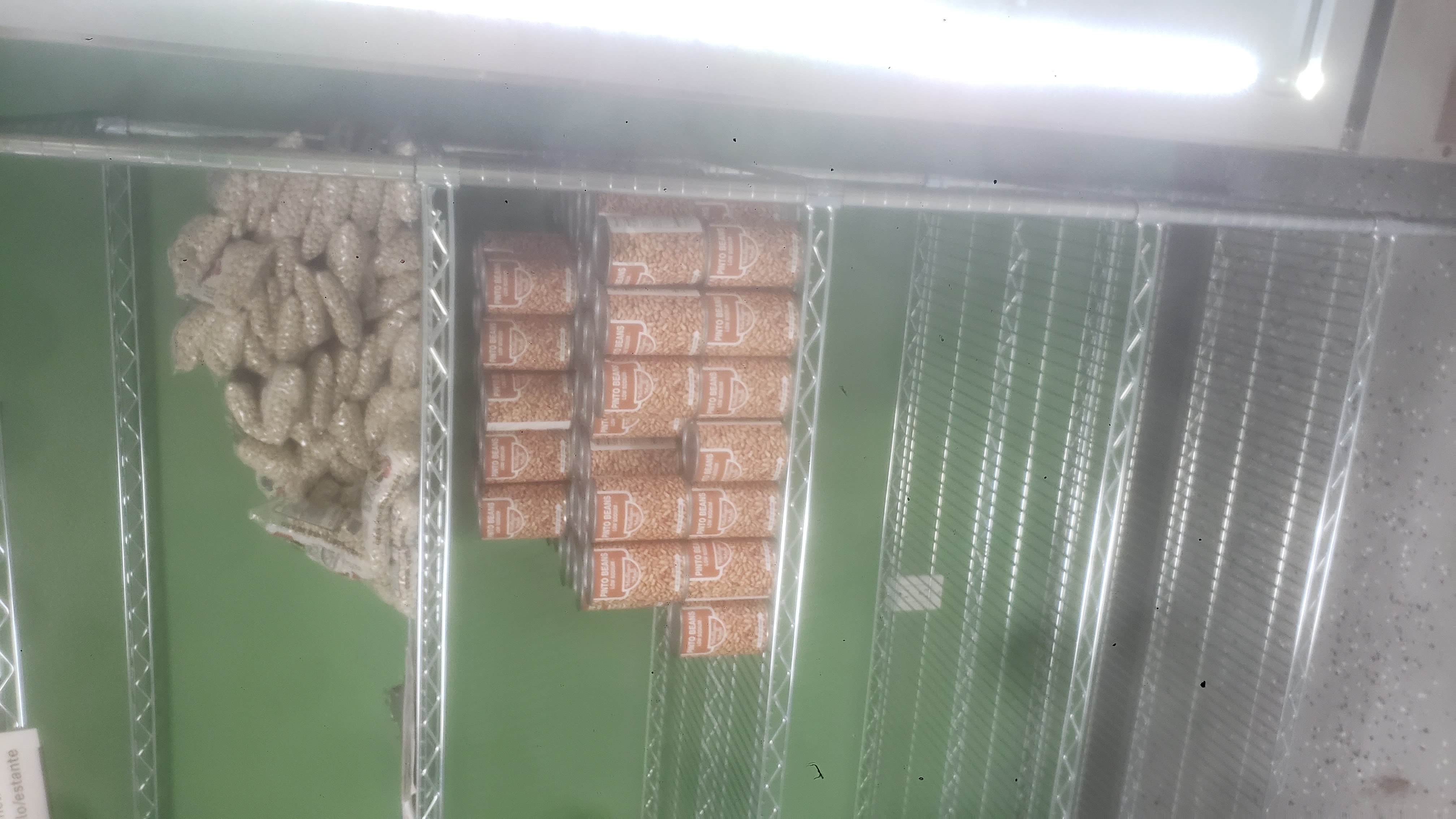 Top shelves of a shelf filled with canned and bags of pinto beans.
